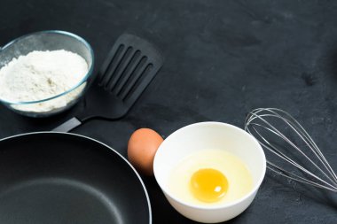 Maslenitsa. Krep yapmak için gerekli malzemeler. Kızartma tavası, yumurta, un, yumurta çırpıcı, siyah arka plan manzaralı. Üst görünüm, metin kopyalanacak yer, tarif.