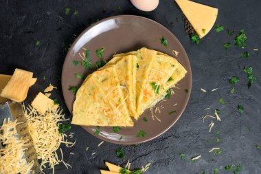 Peynirli gözleme, şifalı ot ve Shrovetide için yumurta. Peynirli tortilla parçalara ayrılır ve üzerine peynir serpiştirilir. Karanlık bir arka planda, en üstteki manzarada. Metin için boşluk.