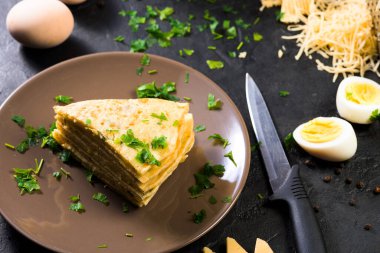 Peynirli gözleme, şifalı ot ve Shrovetide için yumurta. Krep yapmak için gerekli malzemeler. Peynirli tortilla parçalara ayrılır ve üzerine peynir serpiştirilir. Karanlık bir arka planda, en üstteki manzarada. Metin için boşluk.