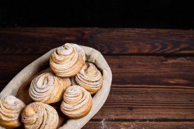 Lezzetli modern çörekler poğaça şeklinde kruvasanlardan yapılır. Tahta kaplamalı tahtadan bir sepetin üzerine pudra şekeri ve ahududu serpiştirilmiş kabuklular. Boşluğu kopyala.
