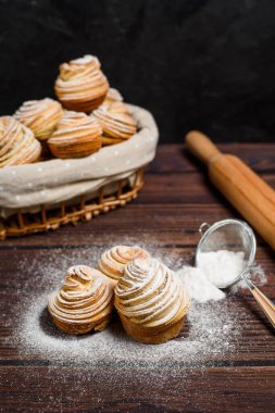 Modern çörekler pofuduk kruvasanlardan yapılır. Çörek şeklinde. Koyu arkaplanda tahta bir sepetin içinde, üzerine pudra şekeri serpiştirilmiş. Uzayı kopyala Yukarıdan görünüm..