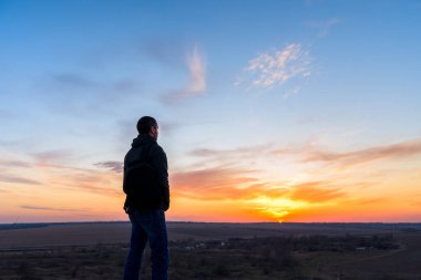 Gün batımında sırt çantalı bir adam bir dağda durup güneşe bakıyor. Hareket özgürlüğü. Bir dağın tepesinde yürümek. Doğadaki vahşi hayat. kamp