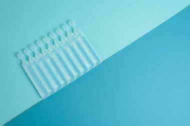 Mavi arka planda şeffaf bir koronavirüs şişesinde sıvı aşı. Yukarıdan manzara. Bir salgında enfeksiyon tedavisi.