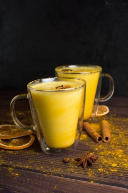 Sağlıklı olmak için şeffaf bardaklarda siyah ahşap bir zemin üzerinde zerdeçal ve bal bulunan altın süt içeceği. Baharatlar, ballı ve baharatlı ılık sütte eritilmiş. Metin için boşluk.