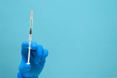 Mavi arka planda Coronavirus 'a karşı elinde mavi eldiven olan bir virüs aşısı. Metin için boşluk. Salgının klinik terapisi. İnsanların sağlığıyla ilgilenmek..