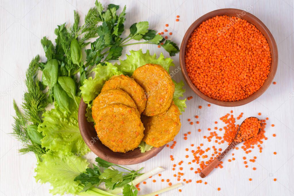 vegetarian meatless cutlets made of lentils and carrots in a wooden plate with vegetables and greens. healthy food. red lentils in a wooden plate on a light background. the view from the top.