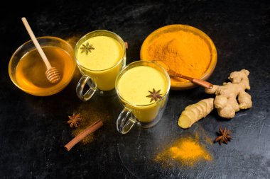 Hint geleneksel altın sütü, zerdeçal, zencefil, baharat, bal. Temiz cam bardaklarda. İçkinin iyileştirici etkisi. Koyu bir arka planda altın bir içecek için malzemeler. Antiviral antioksidan
