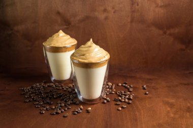 Koyu ahşap arka planda, berrak bardaklarda soğuk dalgona kahvesi. Köpük şeker ve hazır kahve. Soğuk sütün üstünde karıştırıcı var. Kapat. Kore ve Hindistan kremalı kahvesi..