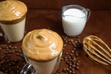 Koyu ahşap arka planda, berrak bardaklarda soğuk dalgona kahvesi. Köpük şeker ve hazır kahve. Soğuk sütün üstünde karıştırıcı var. Kapat. Hint kremalı kahve. Yukarıdan görünüm.