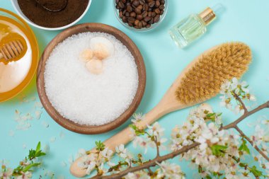 Selülit ve sivilcelerin vücut bakımı için spa ürünleri. Deniz tuzu, kahve fırçası, mavi arka planda tabakta bal ve çiçek dalı. organik bileşenlerin bahar kompozisyonu.