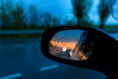 Gün batımında arabanın dikiz aynasında yağmur damlaları. Gün batımı aynaya yansıyor..