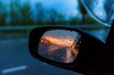 Gün batımında arabanın dikiz aynasında yağmur damlaları. Gün batımı aynaya yansıyor..