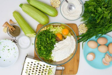 Kabak gözlemesi ve açık arkaplanda yeşillik pişirmek için adım adım tarif. Yanında yumurta, un, sarımsak ve biber de var. Yukarıdan görünüm.