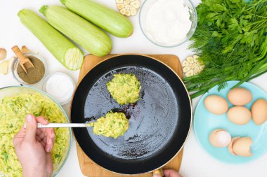 Kabak gözlemesi ve açık arkaplanda yeşillik pişirmek için adım adım tarif. Yanında yumurta, un, sarımsak ve biber de var. Parayı yağlı bir tavaya koy. Yukarıdan görünüm.