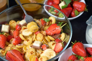 Mini krep gevreği kasesi taze çilekli muz çikolatası, hindistan cevizi talaşı ve küçük tabakta bal. Yukarıdan manzara. Kendini soyutlama eğilimi.