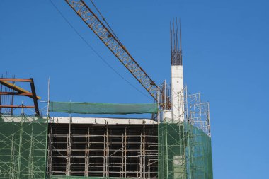 Mavi gökyüzüne karşı vinç ve inşaat alanı. İnşaatın bitmemiş binasının metal inşaatı. Crane kulesi çok katlı depo inşaatı için kullanılıyor.