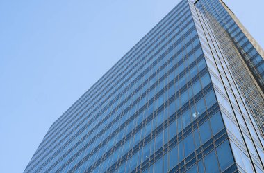 Bir binanın pencerelerinde gökyüzünün yansıması. Mavi gökyüzü üzerindeki modern cam bina gökdelenlerine bakış açısı ve görüş açısı yetersiz. İşyeri pencereleri ya da şirket binası.