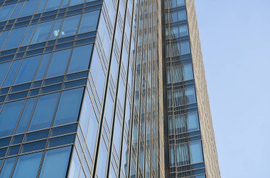 Bir binanın pencerelerinde gökyüzünün yansıması. Mavi gökyüzü üzerindeki modern cam bina gökdelenlerine bakış açısı ve görüş açısı yetersiz. İşyeri pencereleri ya da şirket binası.
