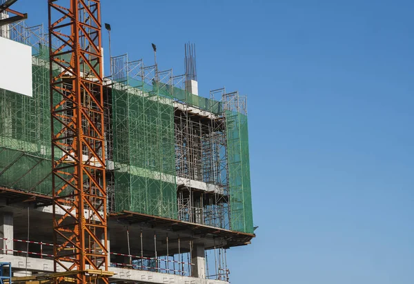 Żuraw i budowa placu budowy przed błękitnym niebem. Metalowa konstrukcja niedokończonego budynku na budowie. Zastosowanie żurawia wieżowego do budowy budynku wielo-magazynowego. — Zdjęcie stockowe