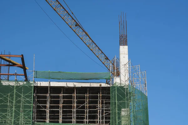 Mavi gökyüzüne karşı vinç ve inşaat alanı. İnşaatın bitmemiş binasının metal inşaatı. Crane kulesi çok katlı depo inşaatı için kullanılıyor.