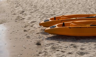 Güneşli bir günde kumlu bir sahilde kürekçilere hazır iki renkli turuncu kano. Kumsalda turuncu renkli tekneler var. Aktif turizm ve su eğlencesi.