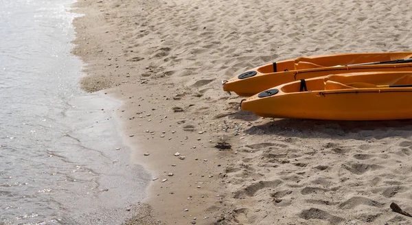 Two colorful orange kayaks on a sandy beach ready for paddlers in sunny day. Several orange recreational boats on the sand. Active tourism and water recreation. — Stock Photo, Image