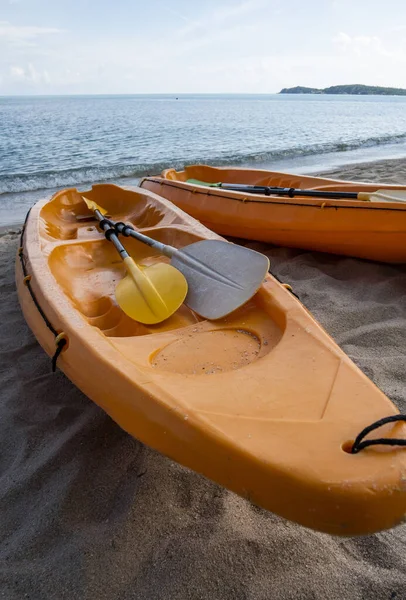 Two colorful orange kayaks on a sandy beach ready for paddlers in sunny day. Several orange recreational boats on the sand. Active tourism and water recreation. — Stock Photo, Image
