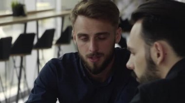 İki neşeli iş adamı bir şey tartışıyor ve kafede dizüstü bilgisayar ve telefonlarla otururken gülümsüyor. İki başarılı genç meslektaşımız, kafeteryadaki organizasyon anlarını teker teker tartışıyor..