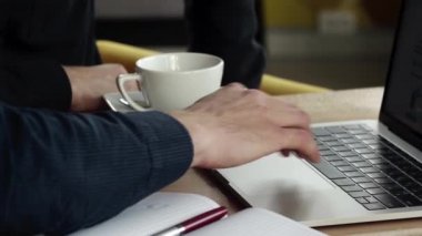 Kafenin ahşap masasında otururken dizüstü bilgisayarda çalışan bir adamın elleri. Kafede dizüstü bilgisayar ve telefonlarla örgütlenmeyi tartışarak..