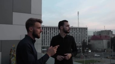 Genç iş arkadaşları gülerek bir şeyler tartışıyor ve akşamları yüksek bir yerde, gün batımında dışarıda dikiliyorlar. İş ortaklığı ya da iş arkadaşı diyaloğu.