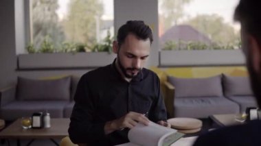 İki neşeli iş adamı bir şey tartışıyor ve kafede dizüstü bilgisayar ve telefonlarla otururken gülümsüyor. İki başarılı genç meslektaşımız, kafeteryadaki organizasyon anlarını teker teker tartışıyor..