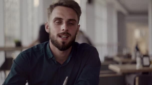 Twee vrolijke zakenmensen die iets bespreken en glimlachen terwijl ze in het café zitten met een laptop en telefoons. Twee jonge succesvolle collega 's in het bespreken van organisatie momenten door tafel in cafe. — Stockvideo