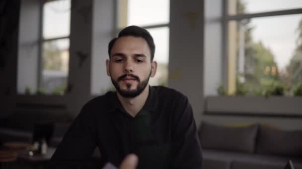 Två glada affärsman diskuterar något och ler medan du sitter på caféet med en bärbar dator och telefoner. Två unga framgångsrika kollegor diskuterar organisationsmoment vid bord på caféet. — Stockvideo