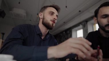 İki neşeli iş adamı bir şey tartışıyor ve kafede dizüstü bilgisayar ve telefonlarla otururken gülümsüyor. İki başarılı genç meslektaşımız, kafeteryadaki organizasyon anlarını teker teker tartışıyor..