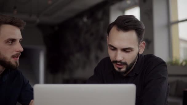 İki neşeli iş adamı bir şey tartışıyor ve kafede dizüstü bilgisayar ve telefonlarla otururken gülümsüyor. İki başarılı genç meslektaşımız, kafeteryadaki organizasyon anlarını teker teker tartışıyor.. — Stok video