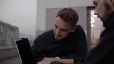 İki iş adamı akşam vakti dışarıda dizüstü bilgisayar ve telefonlarla oturup bir şeyler tartışıyor ve gülümsüyor. Organizasyon anlarını tartışan iki başarılı genç meslektaşım.