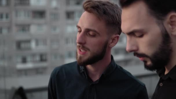 Young businessman coworkers smiling and discussing something together while standing outdoor on a high floor in sunset time in the evening. Business partnership or colleague dialogue. — Stock Video