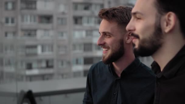 Jóvenes compañeros de trabajo de negocios sonriendo y discutiendo algo juntos mientras están de pie al aire libre en un piso alto en la hora del atardecer por la noche. Colaboración empresarial o diálogo entre colegas . — Vídeo de stock