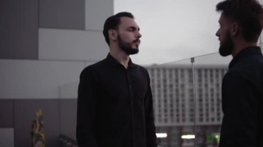 Genç iş arkadaşları akşam vakti dışarıda durup iyi bir diyalogdan sonra el sıkışırken bir şeyi tartışıyorlar. İş ortaklığı ya da iş arkadaşı diyaloğu.