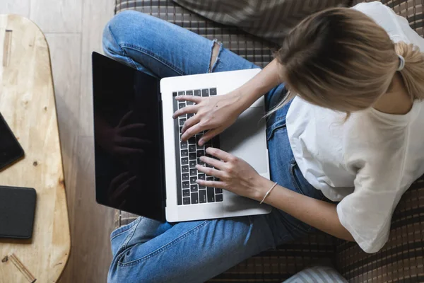 Mujer con una laptop sentada en un sofá. Estudiar y trabajar en línea, freelance. Mujer autónoma, niña que trabaja con su cuaderno sentado en un sofá con un teléfono, smartphone y lector de libros en la mesa . — Foto de Stock