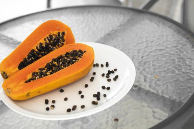 Beyaz bir tabakta tohum ile yarısı kesilmiş papaya. Beyaz arkaplanı olan tatlı papaya dilimleri. Yarım papayalar. Sağlıklı egzotik meyveler. Vejetaryen yemeği..
