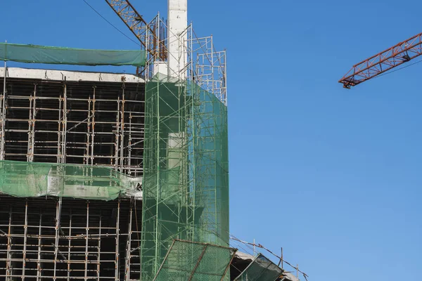 Kräne und Baustelle vor blauem Himmel. Metallkonstruktion des Rohbaus auf dem Bau. Turmdrehkran-Einsatz für den Bau eines Mehrzweckgebäudes. — Stockfoto