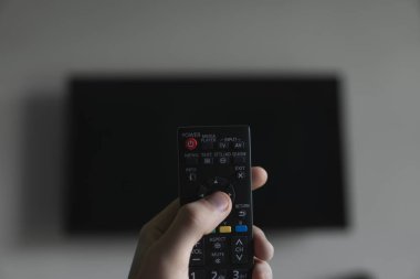 Elinde uzaktan kumanda olan adam Televizyonu açmak istiyor ve uzaktan kumandadaki düğmeye basıyor. El yakın çekimuzaktan uzaktan kumanda.