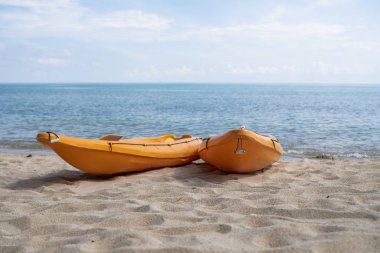Güneşli bir günde kumlu bir sahilde kürekçilere hazır iki renkli turuncu kano. Kumsalda turuncu renkli tekneler var. Aktif turizm ve su eğlencesi.