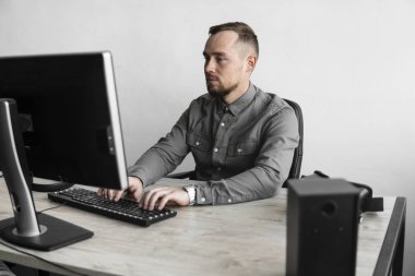 Genç işadamı ya da öğrenci bilgisayar monitörü karşı oturan bir gömlek. Düşünceli bir ifade ile ofiste bir masada bir pc üzerinde çalışıyor. Ofiste dizüstü bilgisayar üzerinde çalışan genç işadamı.