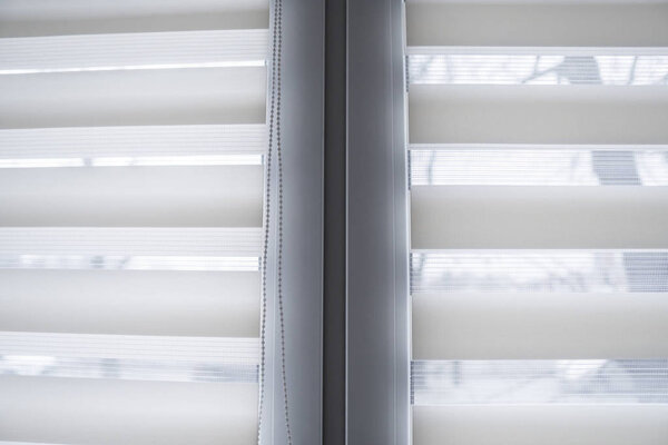 Details of white fabric roller blinds on the white plastic window in the living room. Close up on roll curtains indoor.