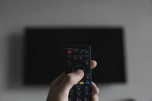 Ο άνθρωπος με το τηλεχειριστήριο στο χέρι θέλει διακόπτη στην τηλεόραση και πιέζει το κουμπί στο τηλεχειριστήριο. Τηλεχειρισμός στο χέρι κοντινό πλάνο. — Φωτογραφία Αρχείου