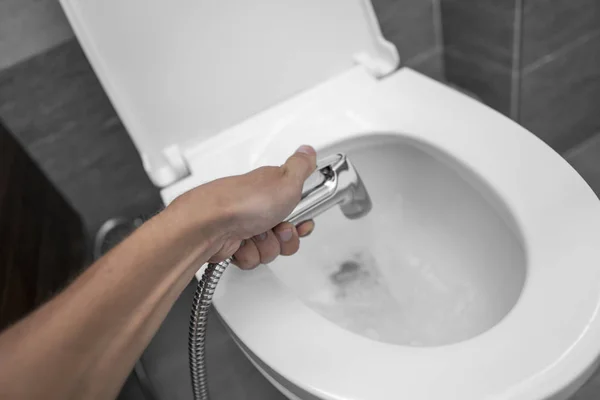 Použití bidetové sprchy s bílým WC. Bidet sprcha v mužské ruce pro použití s bílou toaletní mísou. — Stock fotografie