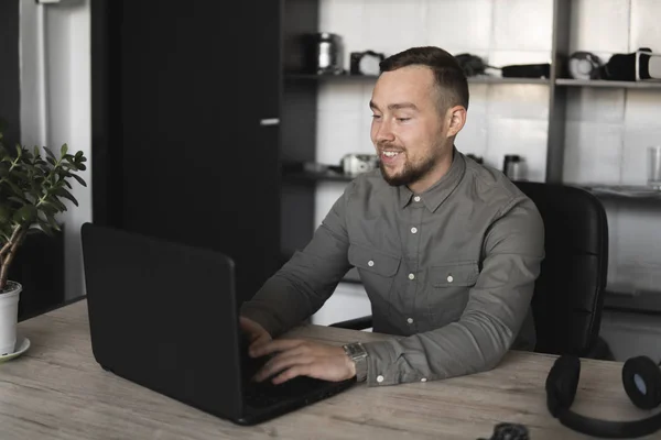 快乐微笑年轻的商人或学生穿着衬衫坐在电脑显示器上。在办公室的桌子上用一张电脑，用深思熟虑的表情. — 图库照片