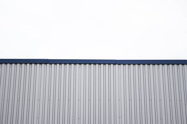 Mavi metal köşeli bir binanın metal kıvrımlı levhaları. Fabrikaların ve sanayi binalarının arka planında bulutlu gökyüzüne karşı beyaz alüminyum metal kıvrımlı çatı veya duvar levhaları.